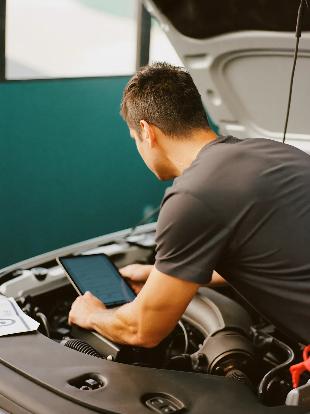 Photograph of an independent local operator inspecting and photo-documenting a car's engine bay with a tablet.